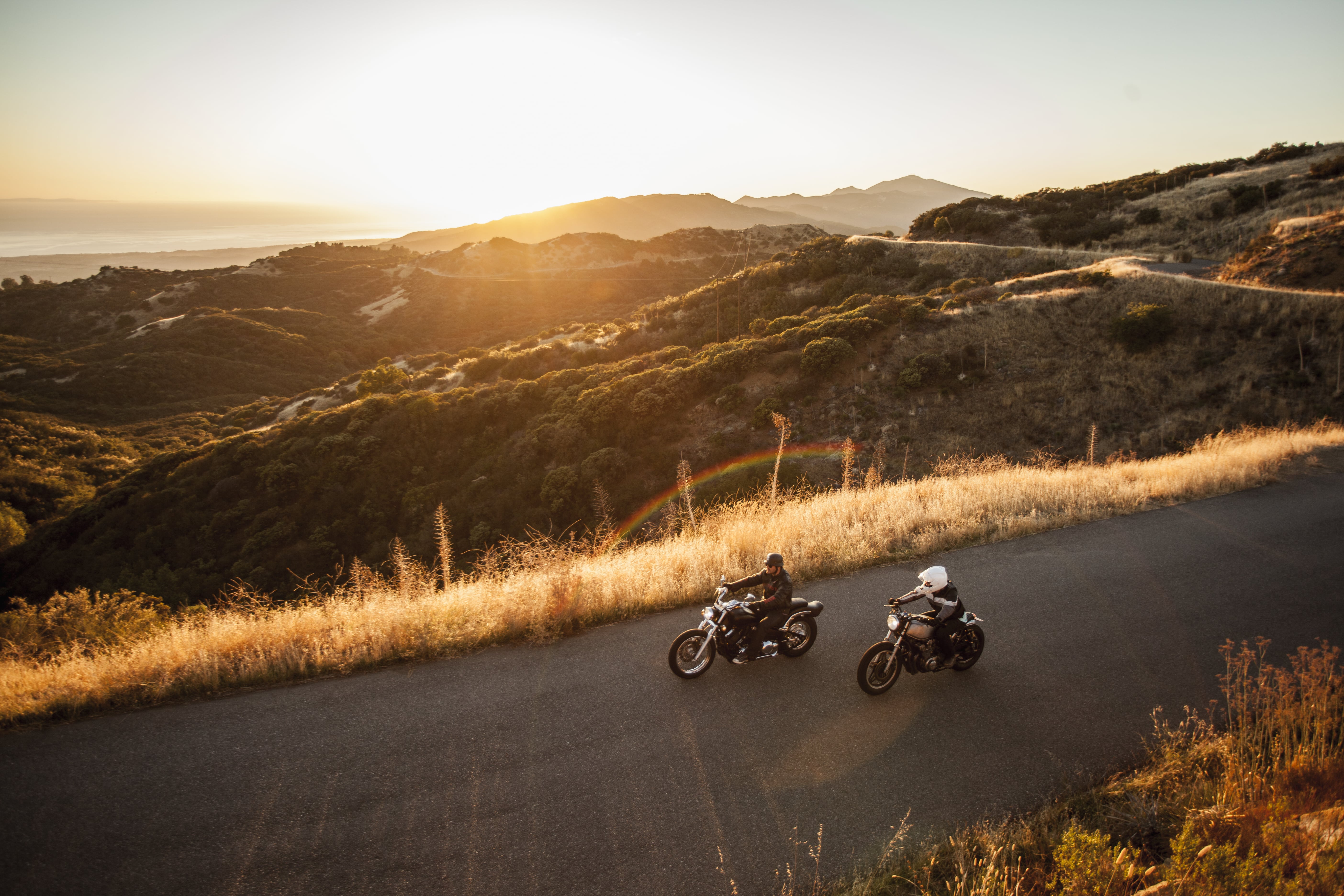 Two people on motorcycles riding on a road overlooking mountains 