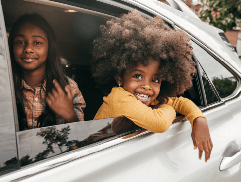 Two kids smiling in the back of a silver car