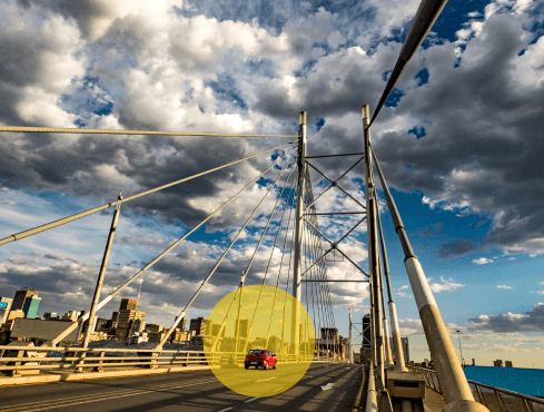 A small red car driving on a bridge on a blue sky day