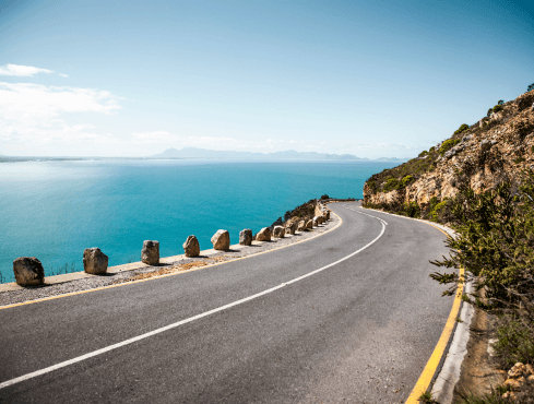 A curving road with a beach and a mountain in view